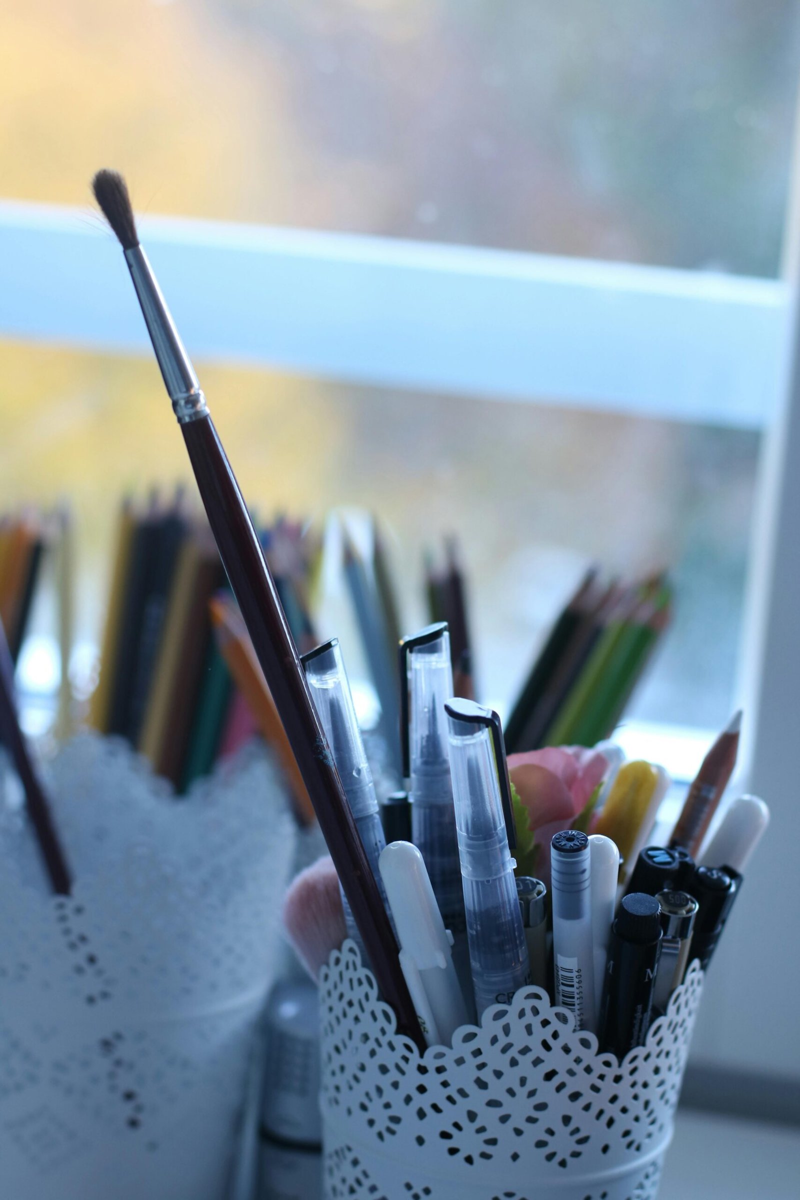 A collection of pens and brushes in decorative containers by a window.